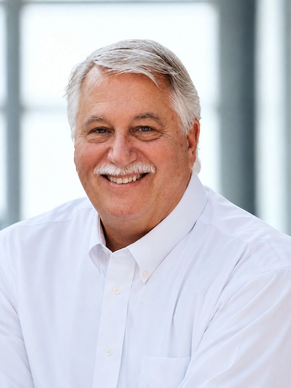 Smiling elderly man with white hair and mustache in white shirt.