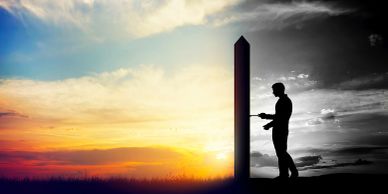 Silhouette of a man touching a tall monolith at sunset.