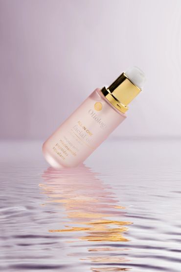 Pink skincare bottle with gold cap reflected on water surface.