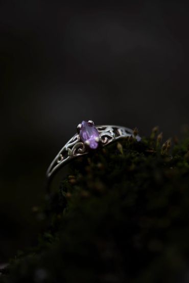 Silver ring with purple gemstone on moss.