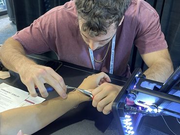 Person tattooing another person's wrist with a lighted lamp.