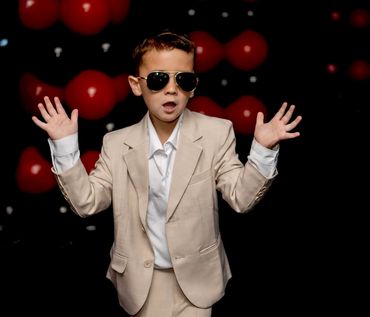 Young boy in beige suit with sunglasses posing.