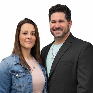 Smiling man in black blazer and woman in denim jacket posing.
