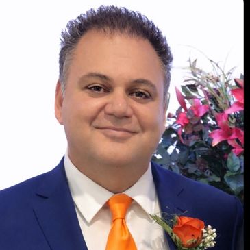 Man in a blue suit with an orange tie and boutonniere smiling.