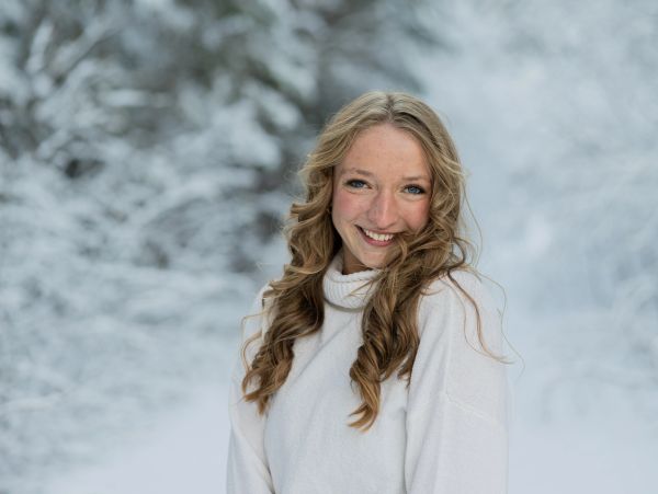 A smiling woman in a white sweater outdoors in the snow.