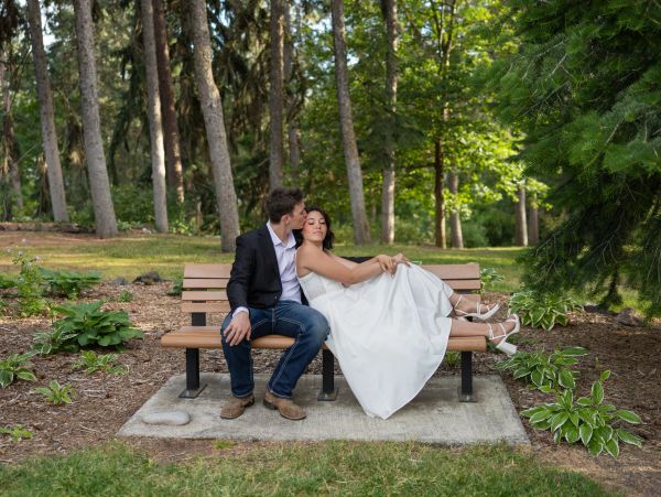 Newlyweds sitting on a bench in a park, sharing a tender moment.