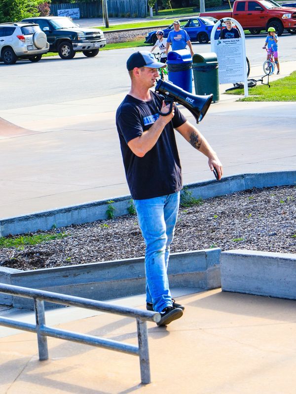 Man with a megaphone at a skate park with kids in the background.