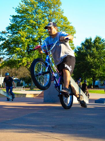 Man performing a BMX bike trick at a skatepark on a sunny day.