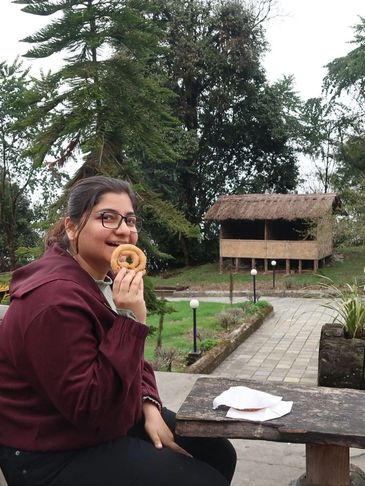 A woman enjoying a snack outdoors near a rustic hut.