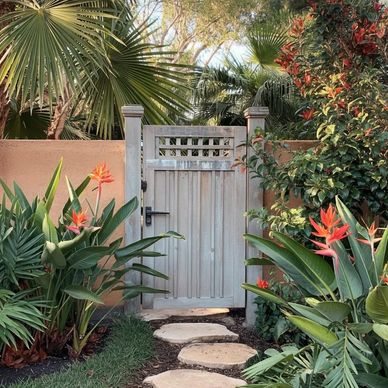 Wooden garden gate surrounded by tropical plants and stone path.