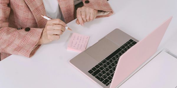 Person writing on a sticky note next to a laptop.
