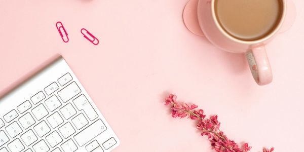 A pink-themed workspace with a keyboard, coffee cup, paper clips, and pink flowers.