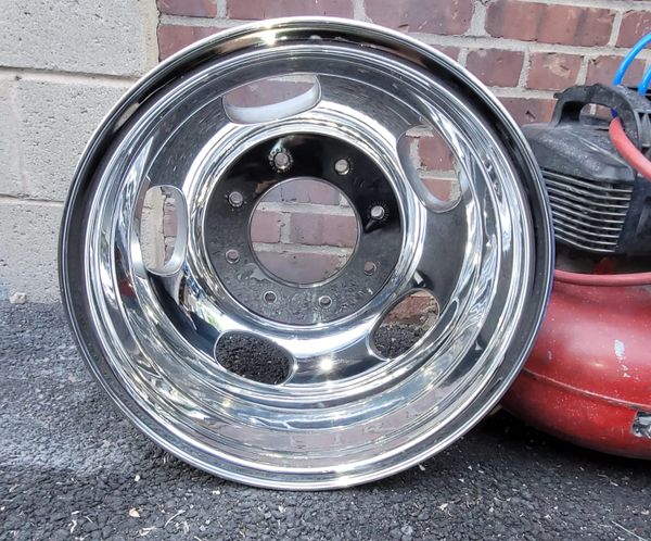 Shiny chrome wheel rim leaning against a brick wall outdoors.