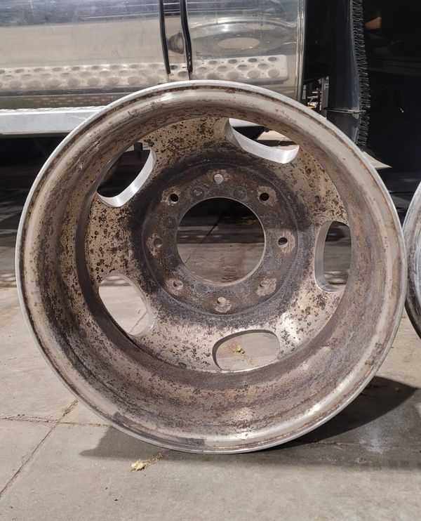 Rusty, dirty vehicle rim resting on a concrete floor.