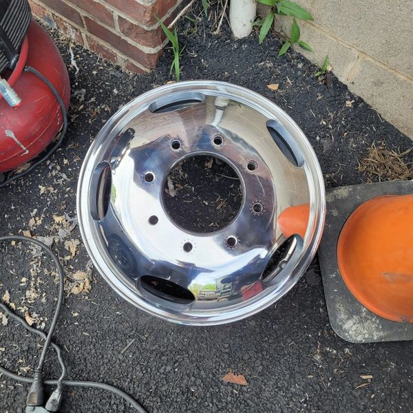 Shiny chrome truck wheel hubcap on asphalt near orange cone and red air compressor.