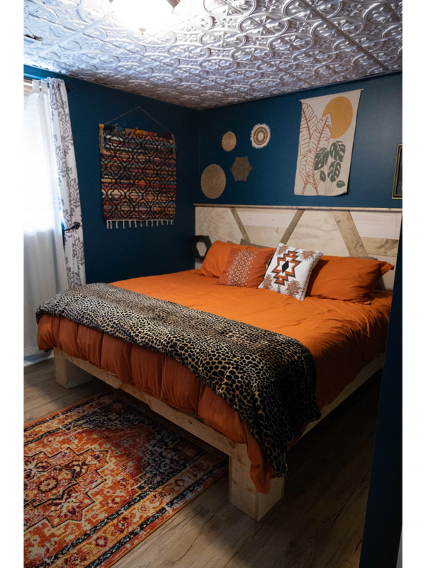 Cozy bedroom with orange bedding and blue walls accented by woven wall art and patterned rug.