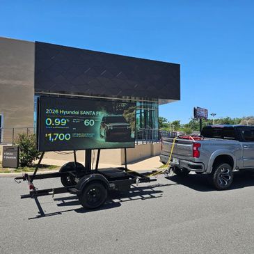 Pickup truck towing a trailer with an LED advertising screen for Hyundai Santa Fe.