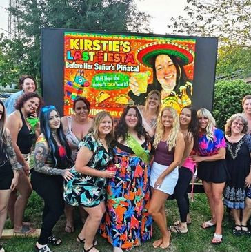 Group of women celebrating a fiesta-themed party outdoors with a colorful sign.