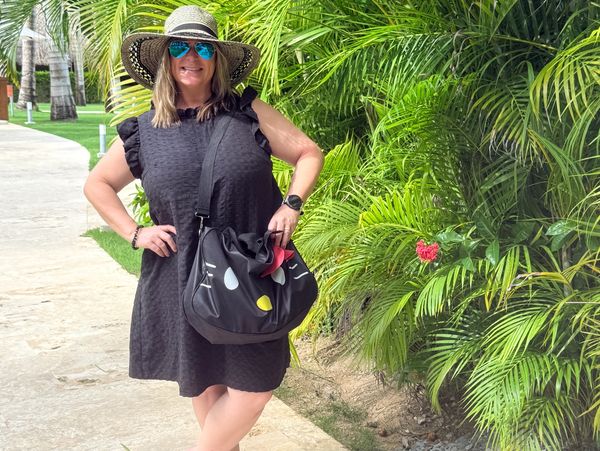 Woman in black dress and sunhat posing near green palm leaves.