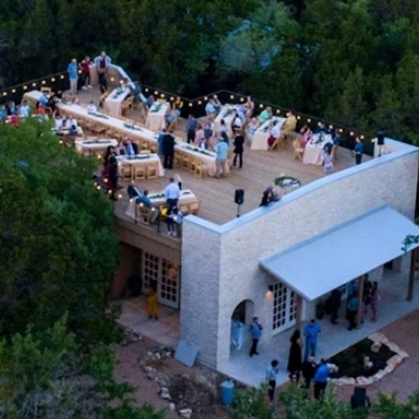 A rooftop party with guests surrounded by trees at dusk.