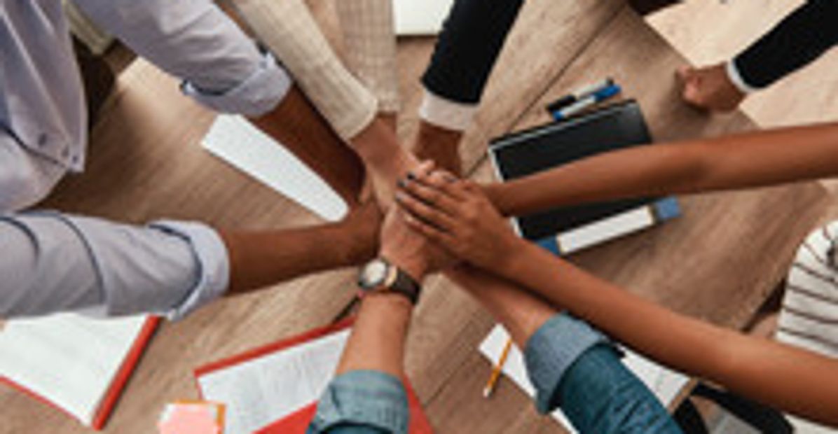 Team members joining hands in a collaborative gesture over a desk.