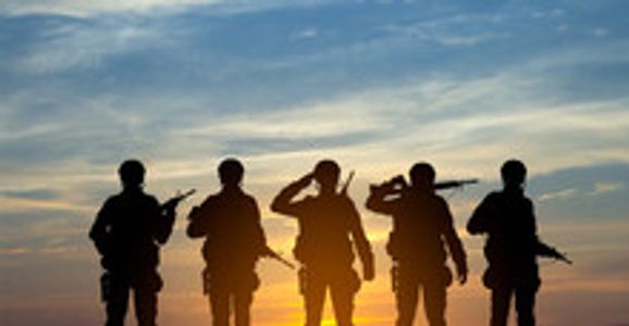 Silhouettes of five soldiers saluting at sunset.