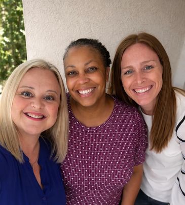 Three smiling women posing closely for a cheerful photo.
