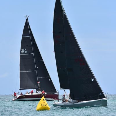Two sailboats with black sails rounding a race mark. 