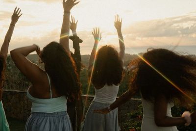 Three women enjoying a sunset outdoors with arms raised.