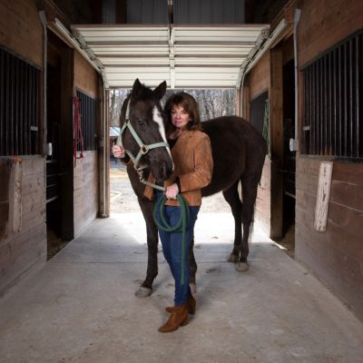 Woman standing with a horse inside a stable.