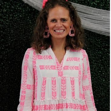Woman smiling in white and pink dress with matching earrings.