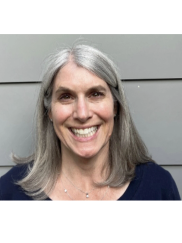 Smiling woman with gray hair against a gray wall.