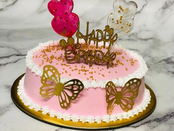 Pink birthday cake with golden butterflies and decorative balloons.