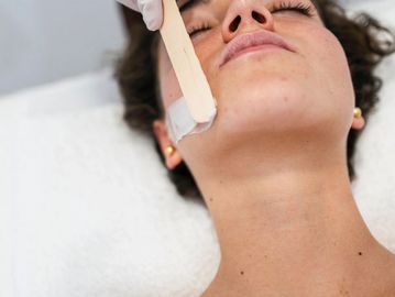 Full face waxing treatment removing facial hair from chin with professional wax application