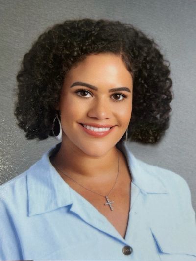 Young woman with curly hair smiling in a light blue shirt.