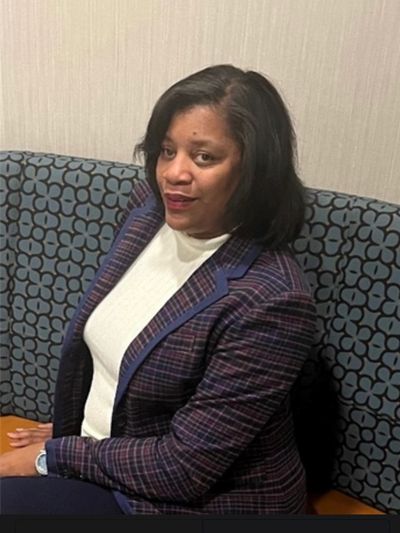 Woman in plaid blazer and white top sitting on patterned bench.