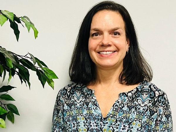 Smiling woman with dark hair in patterned blouse near green plant.