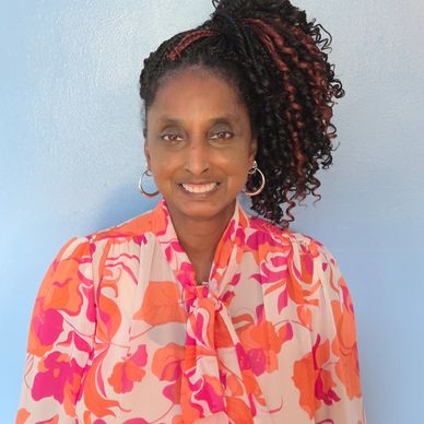 Smiling woman with curly hair and colorful blouse.