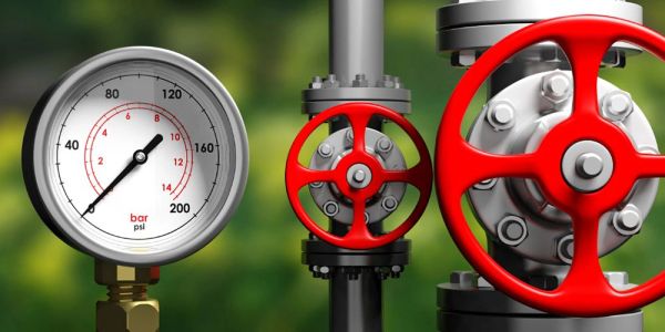 Pressure gauge and red valve wheels on pipes.