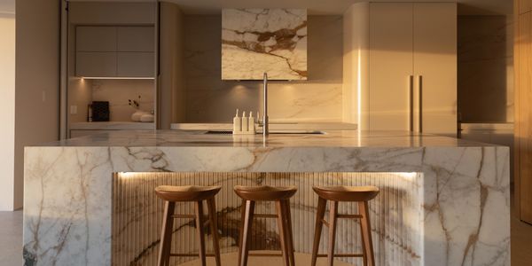 Elegant kitchen with marble island and wooden stools, bathed in warm natural light.