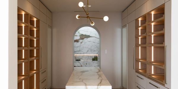 Modern kitchen with marble island and illuminated wooden shelves.