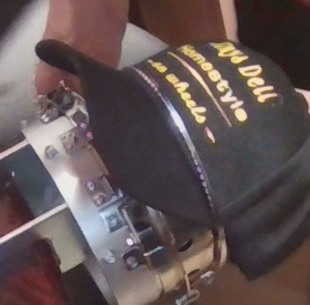 Person wearing a black hat with text and holding a tambourine.