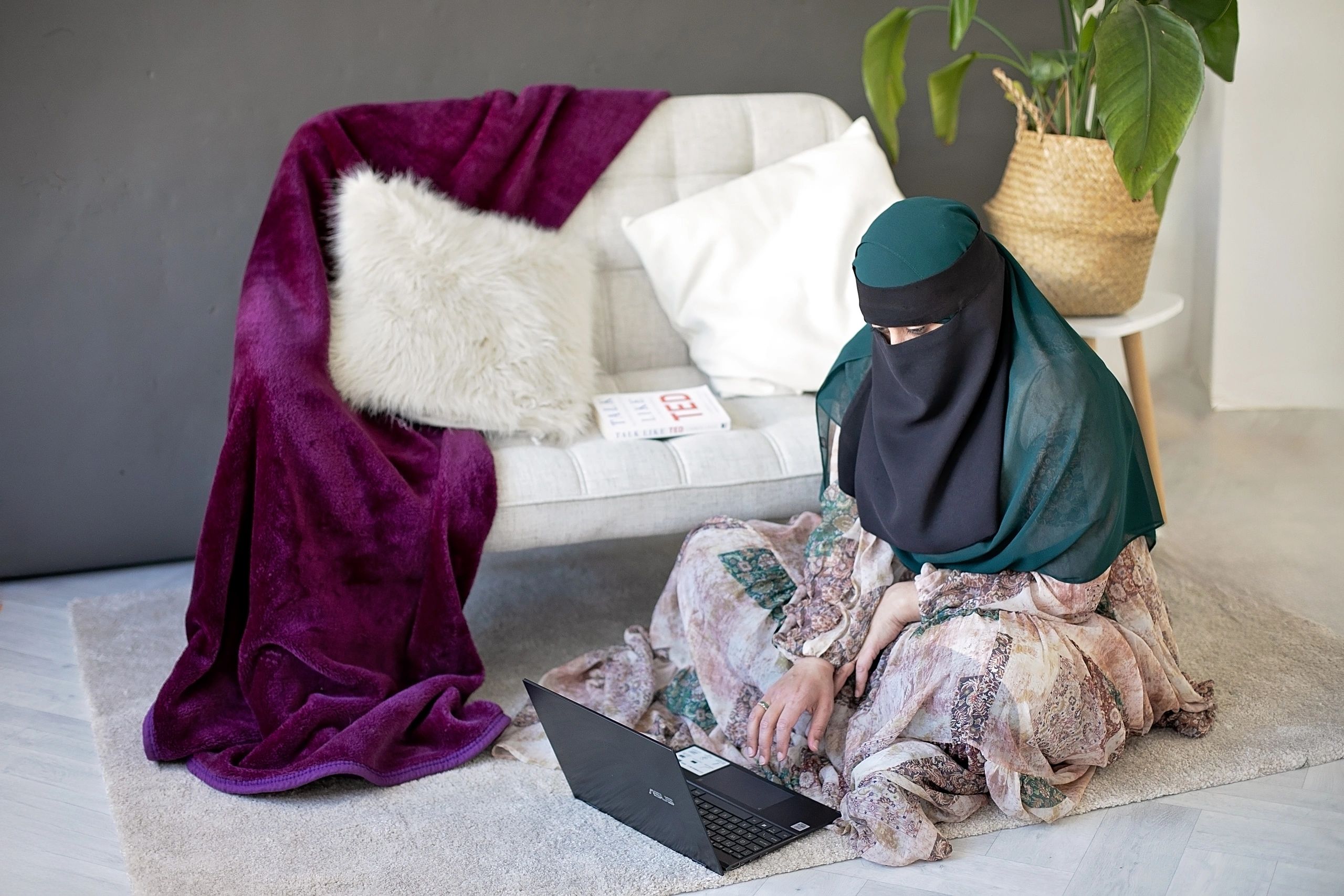 Woman wearing a hijab using a laptop at home.