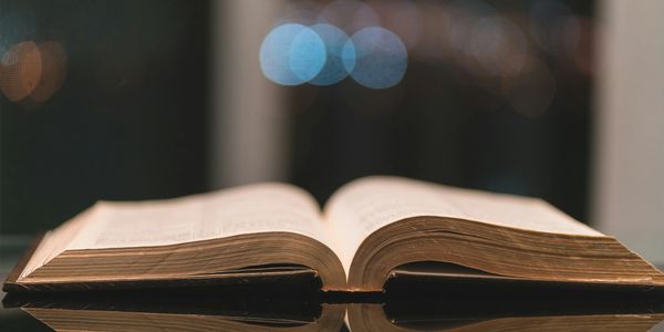 Open book reflecting on a shiny surface with blurred lights in the background.