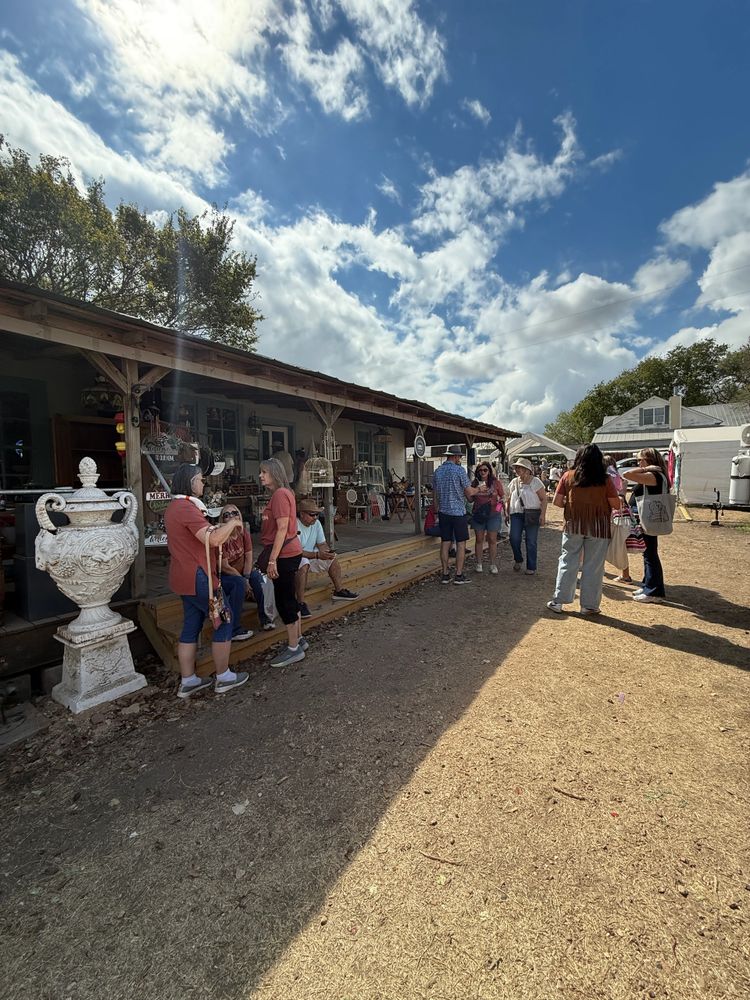 People socialize outdoors near a rustic building under a partly cloudy sky.