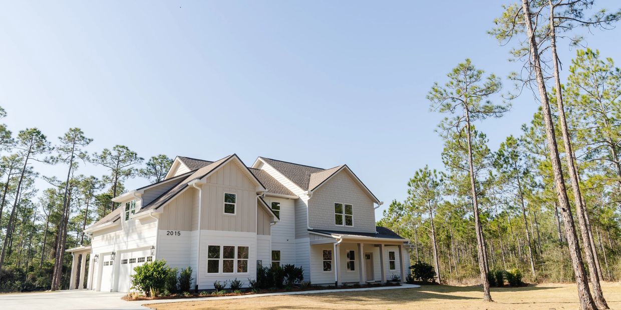 Modern two-story house surrounded by tall pine trees under clear sky.