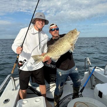 Two men on a boat proudly holding a large fish they caught.