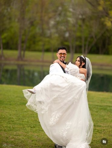 Groom carrying bride outdoors on wedding day.