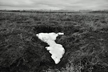 A patch of melting snow on dark, barren ground in a bleak landscape.