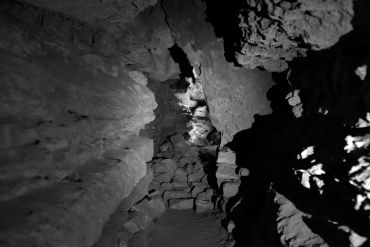 Dimly lit narrow cave passage with rocky walls.